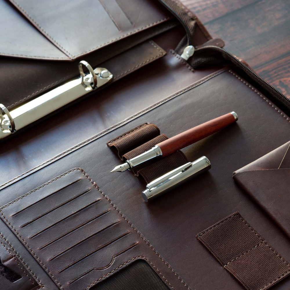 Un stylo-plume en bois Hörner Legno avec sa plume visible, dévissé sur un porte-documents de conférence en cuir brun