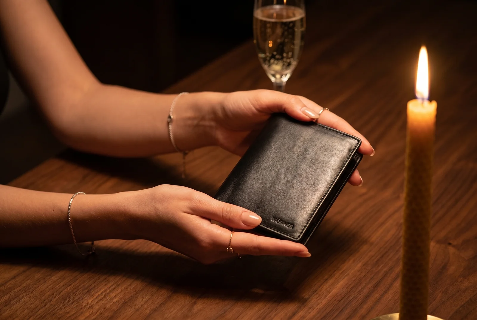Unas manos sostienen una cartera Hörner durante una cena de cumpleaños, con una copa de champán y una vela