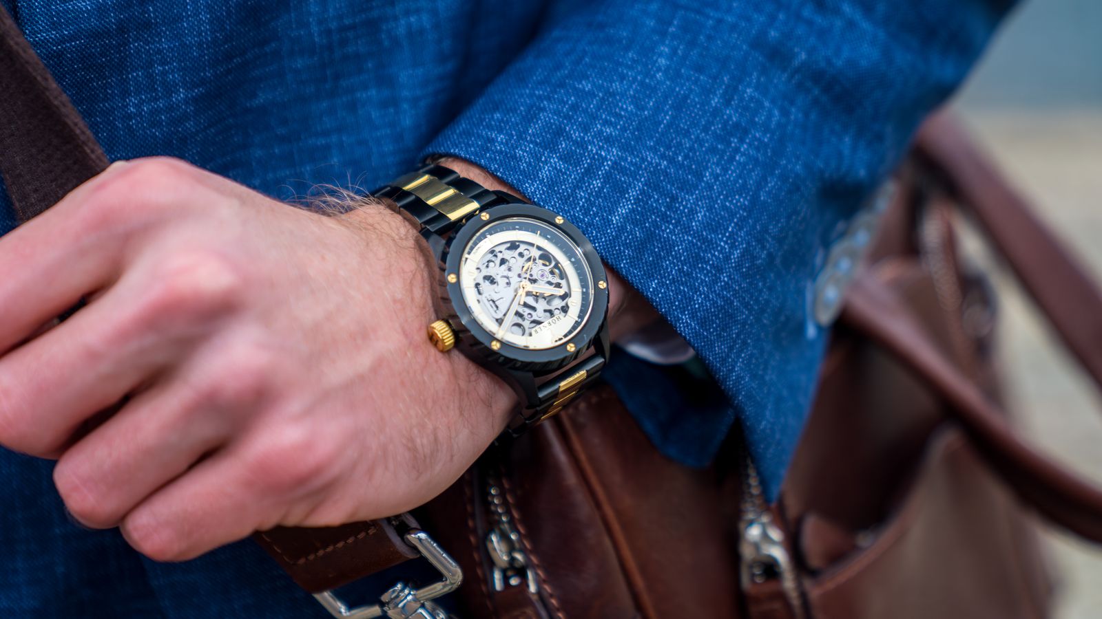 Reloj automático Pulsar de Hörner con mecanismo esqueletizado en la muñeca, llevado con una americana azul junto a un bolso de cuero, como regalo de selectividad