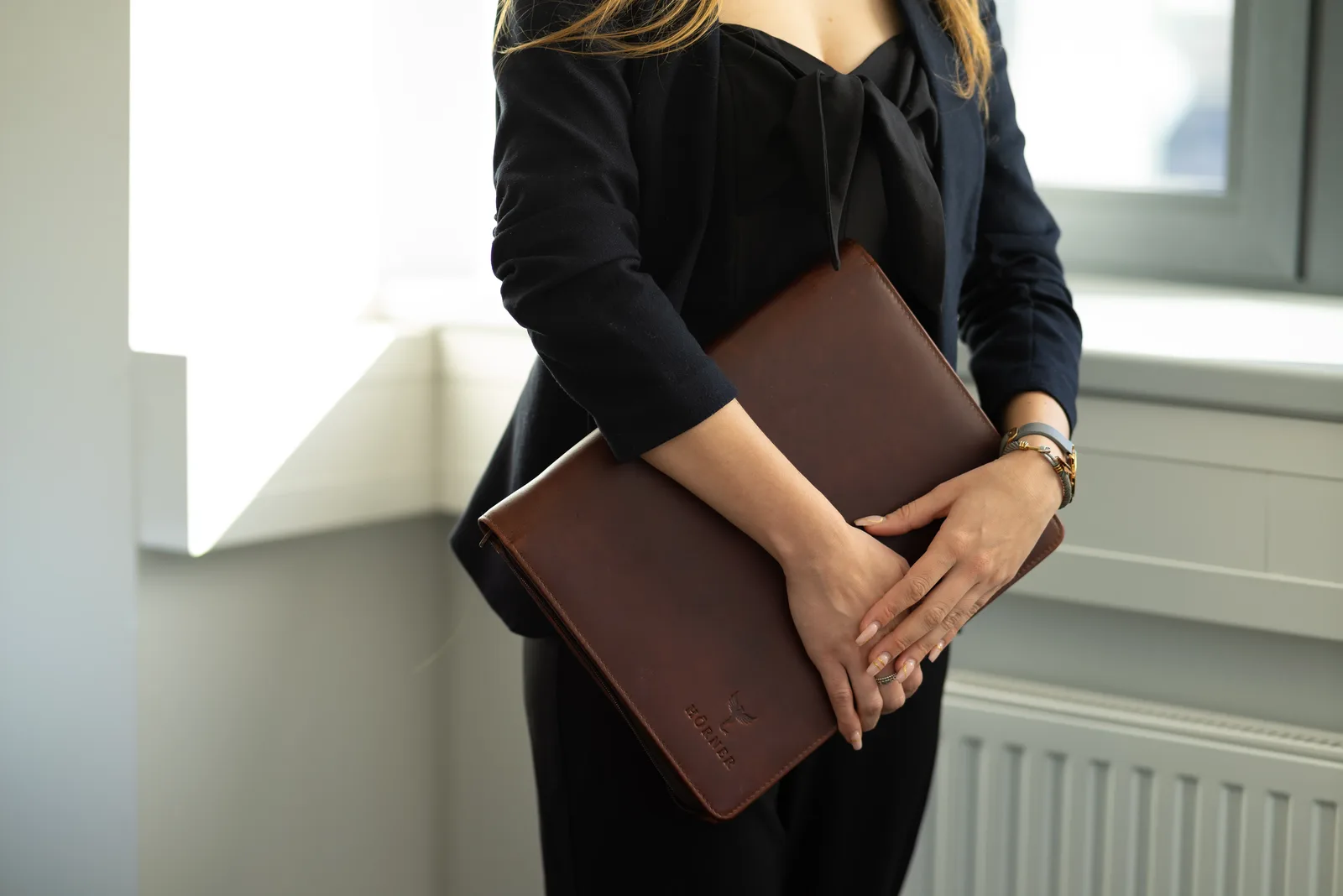 Persona sosteniendo la carpeta de conferencias Hörner Berlin de cuero Cognac junto a una ventana luminosa