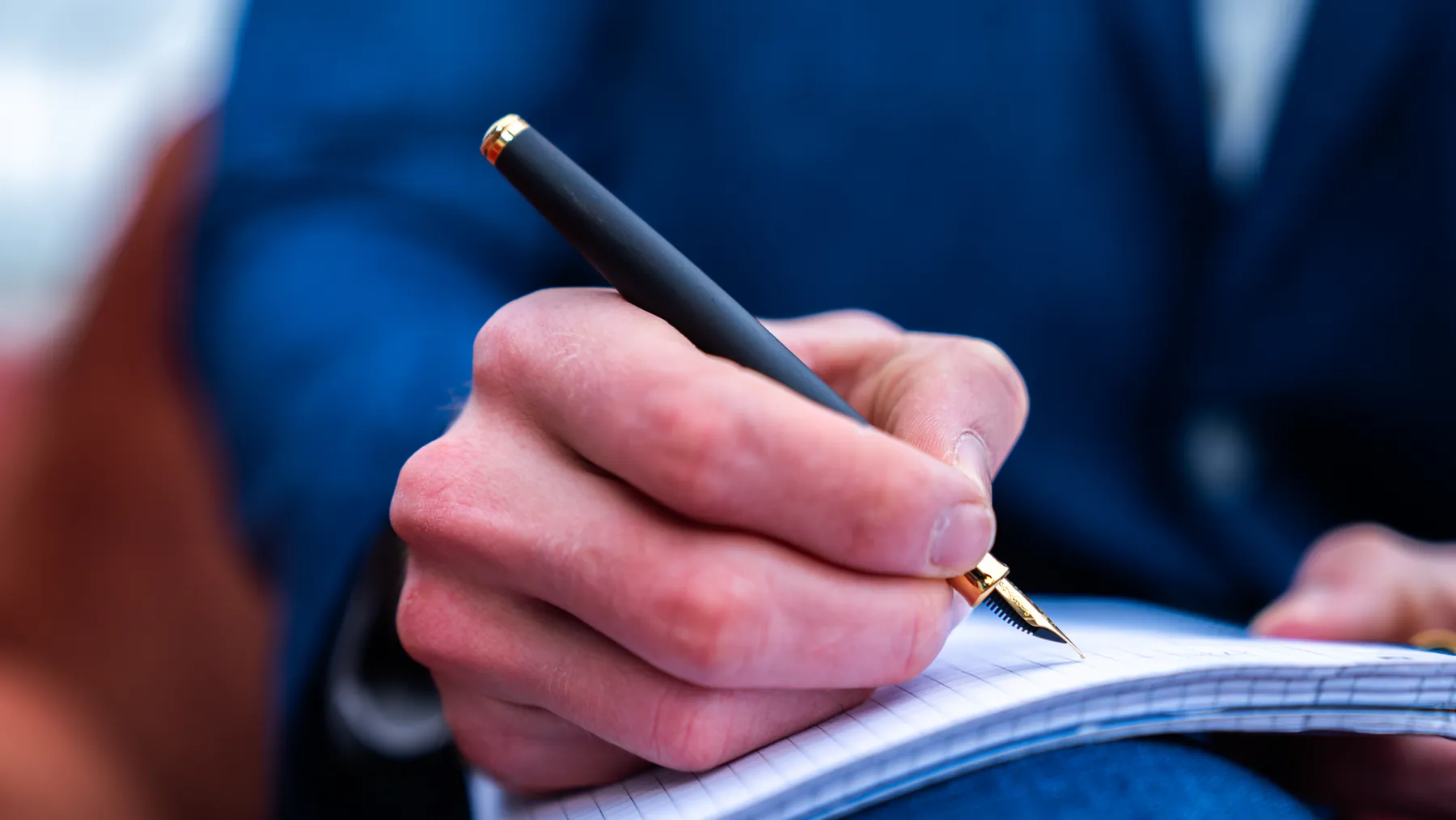 Main écrivant avec un stylo-plume Hörner noir et or dans un carnet à carreaux